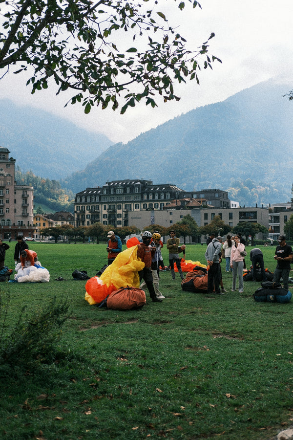 People preparing paragliders on a grassy field