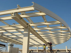 Two construction workers build a large white steel canopy structure.